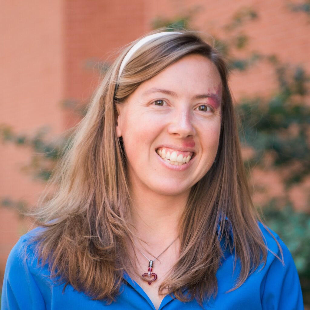Portrait of smiling woman with long hair, wearing a headband, collared dress shirt, and necklace.