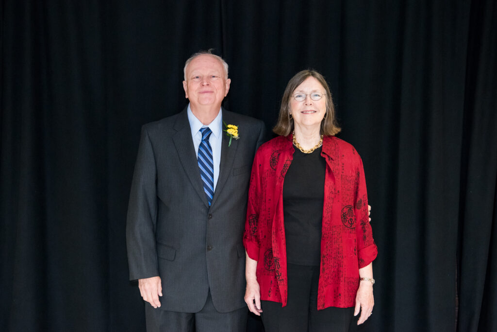 Man in suit with blue striped tie standing next two woman in black top and pants and flowing red jacket