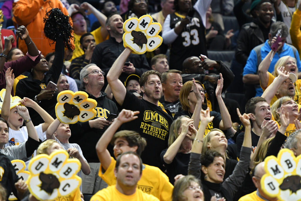 Fans cheering, holding and wearing UMBC fan gear.