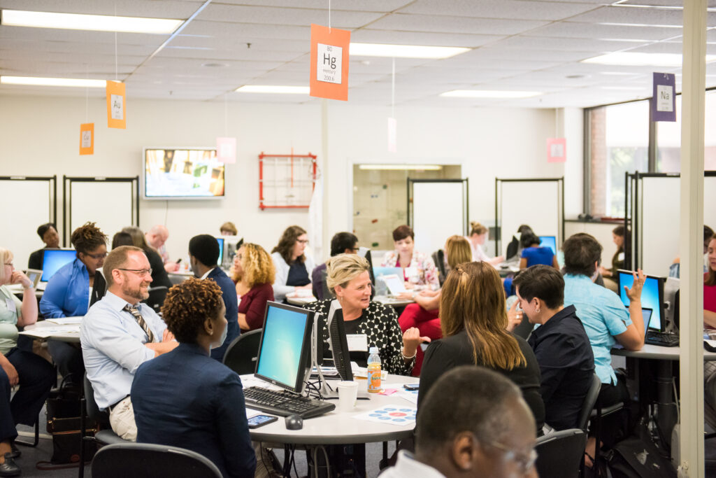 University professionals sit around table with computers, talking to one another.
