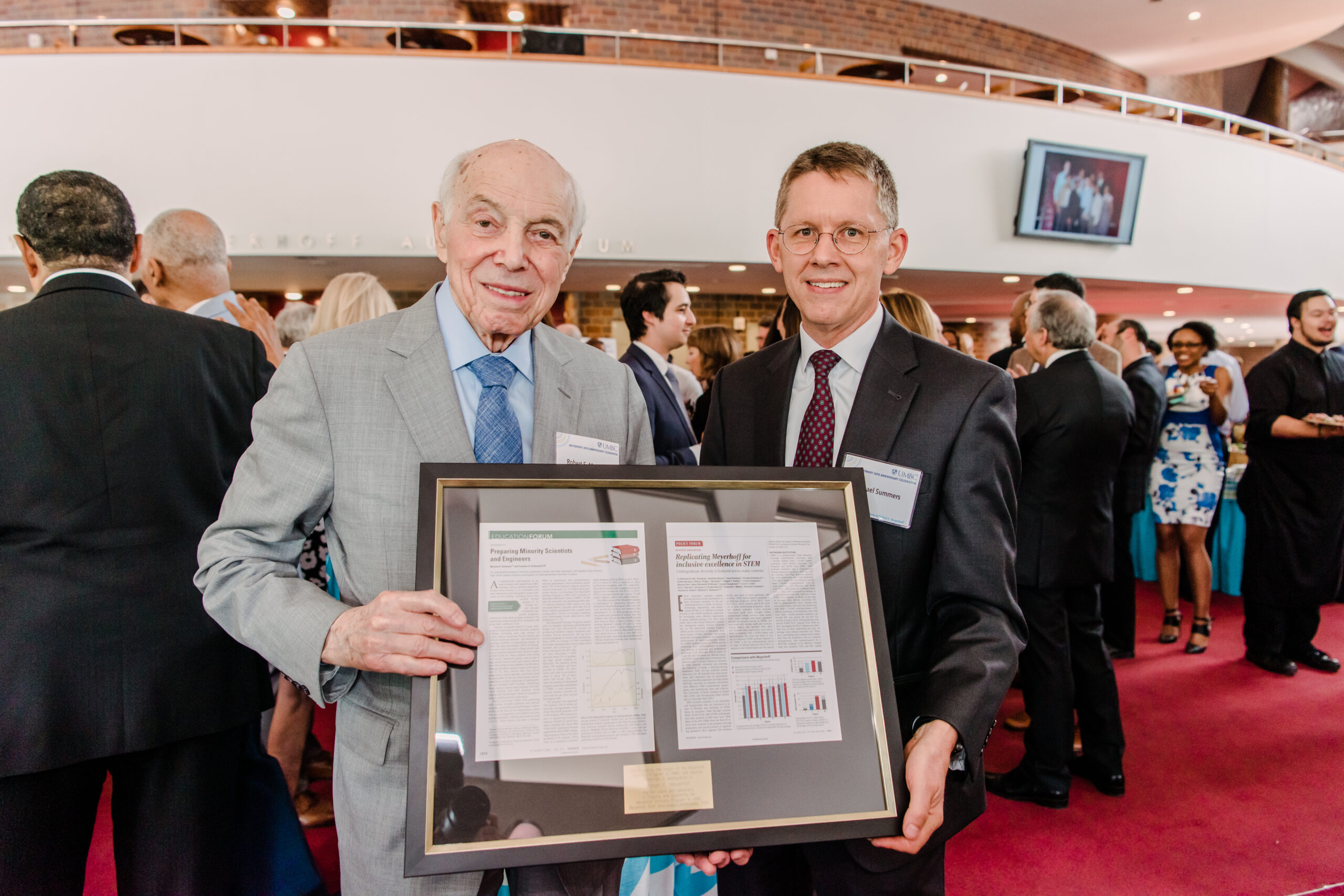 Summers holds framed newspaper with man at Meyerhoff Scholars Program