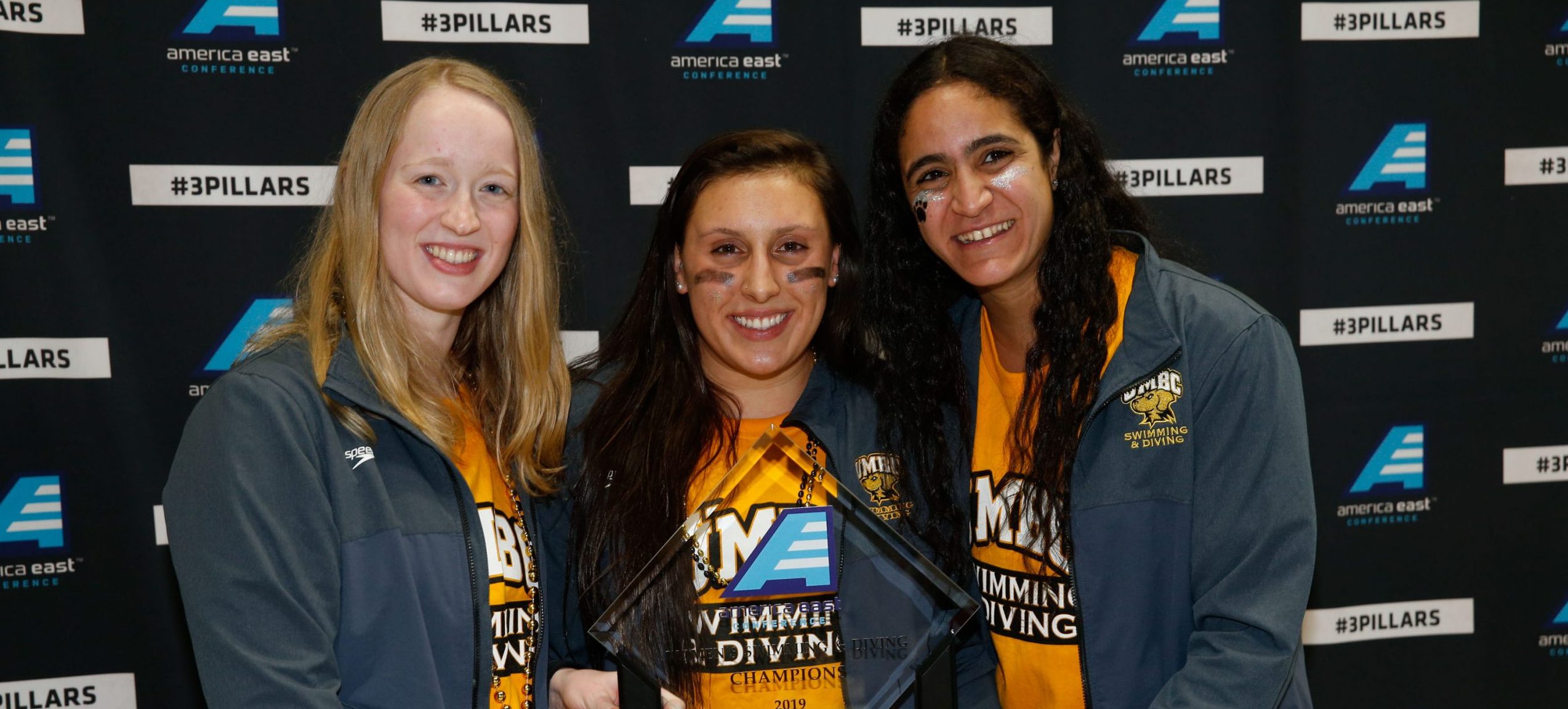 Three girls holding America East trophy.