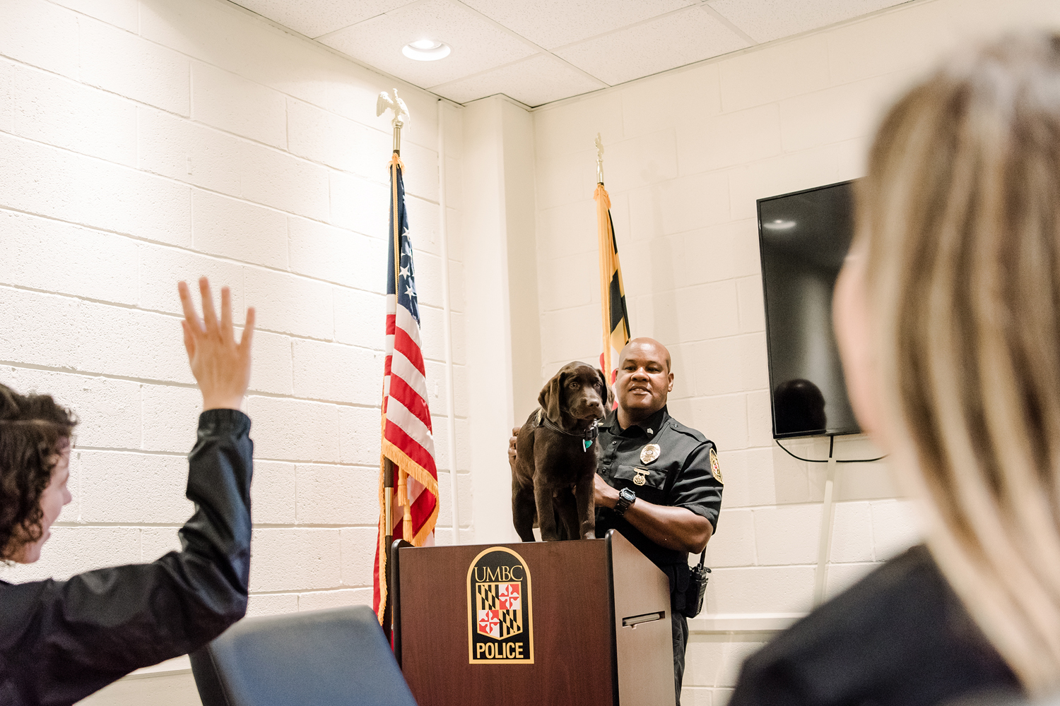 Sergeant Cheatem stands UMBC Police comfort dog on a podium