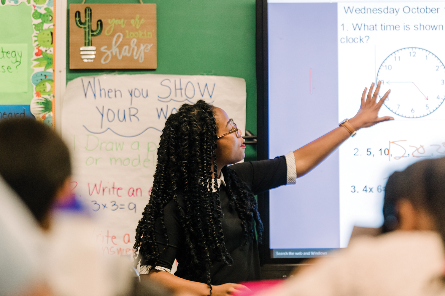Lydia Coley points to a whiteboard with a clock on it