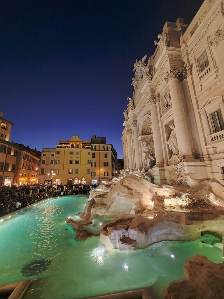 Crowd at the glowing Trevi Fountain.