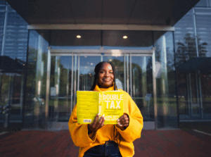 Writer Anna Gifty Opoku-Agyeman holdinh her book "The Double Tax: How Women of Color are Overcharged and Underpaid" (Credit: Corban Swain Productions).