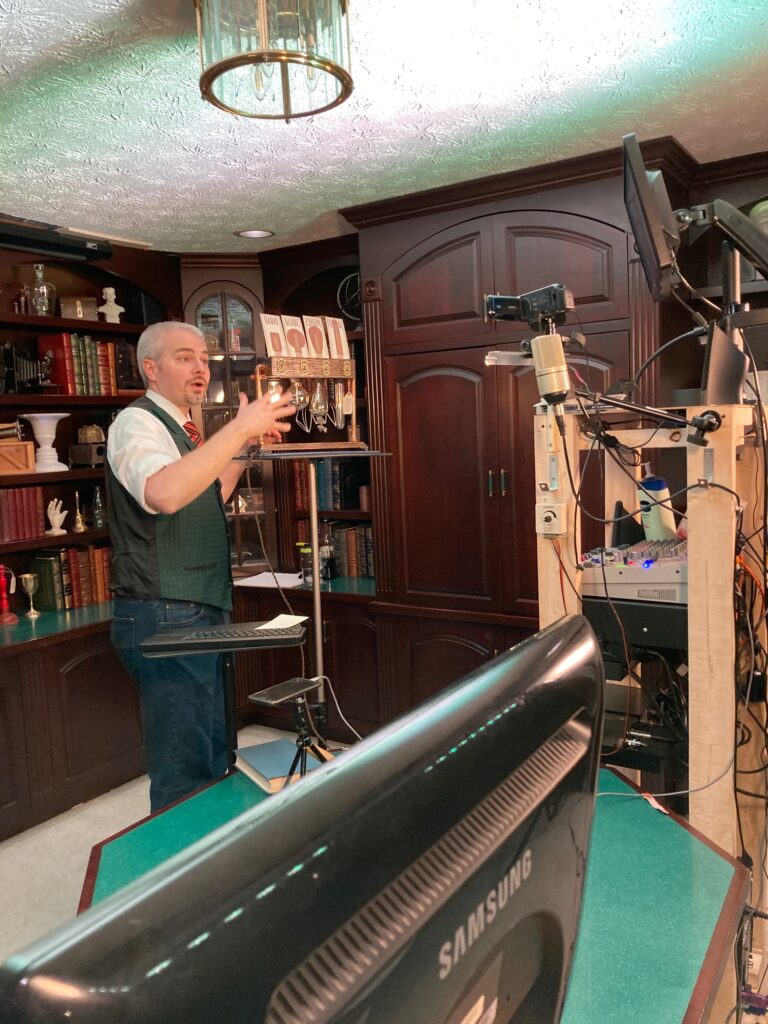 a man performs magic at a stand up desk for an online audience