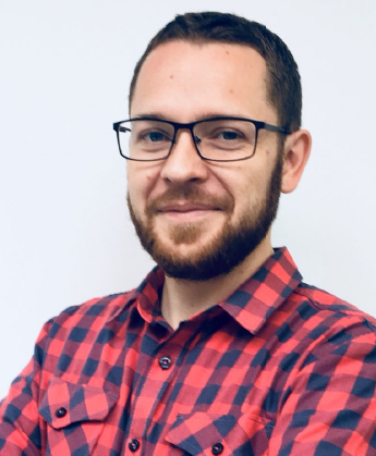 A young man with short cropped hair wearing black rimmed glasses and a checkered corral and blue shirt.