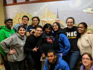 A group of eleven young men and women huddling together in front of a mural.