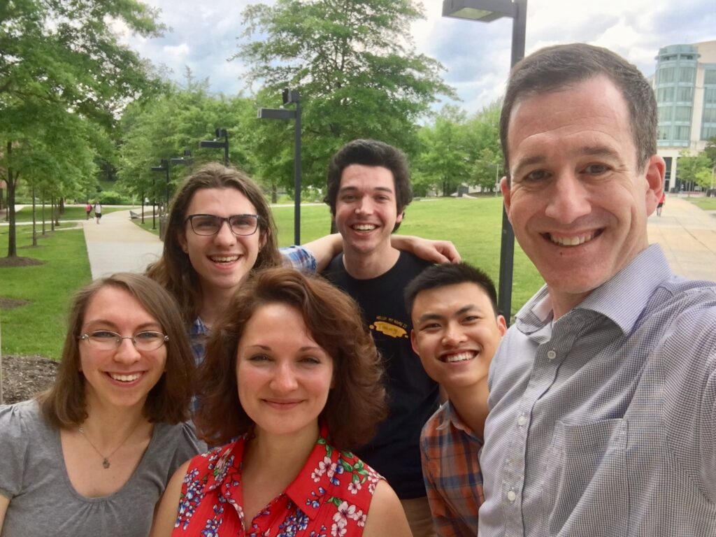 A group of five people stands for a selfie outdoors, smiling.