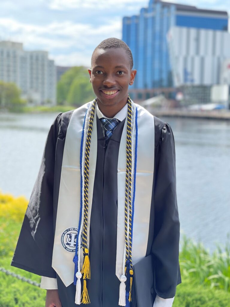 Young man smiles for a portrait, wearing graduation regalia.