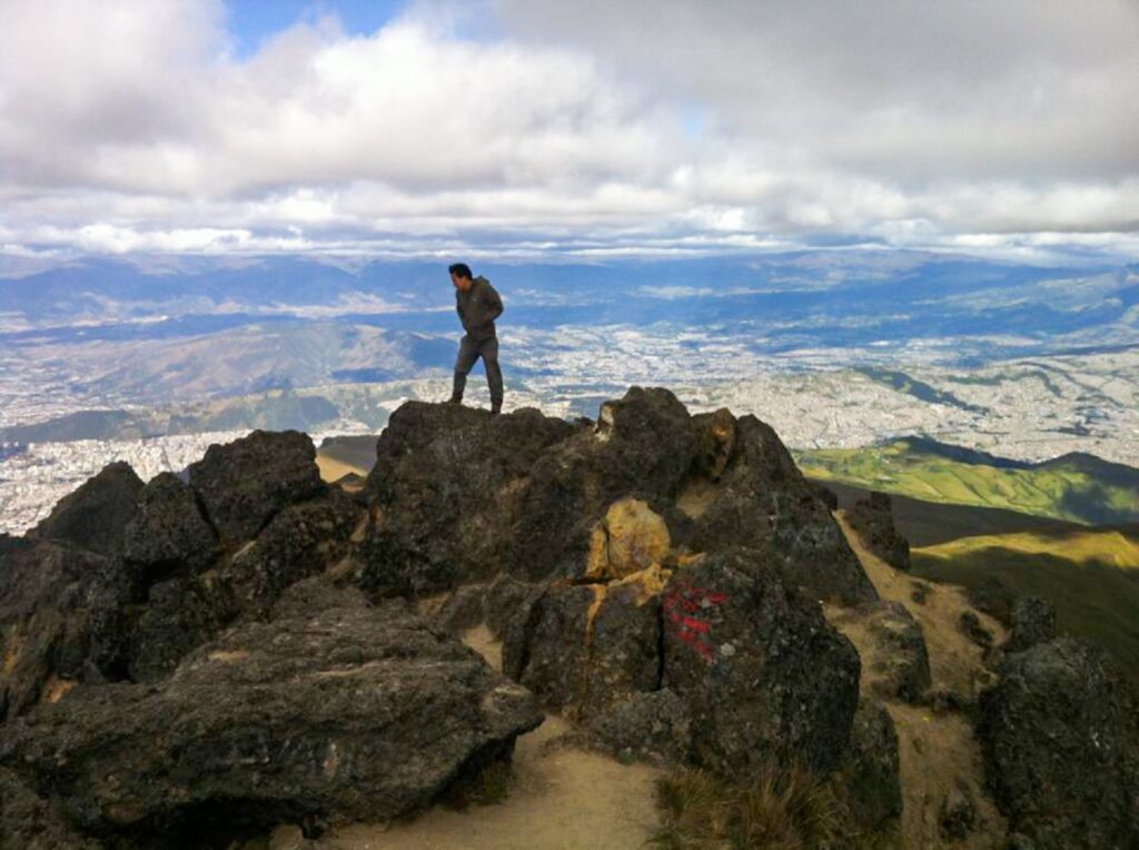 A man walking along the ridge of a mountain with a cityscape behind him.