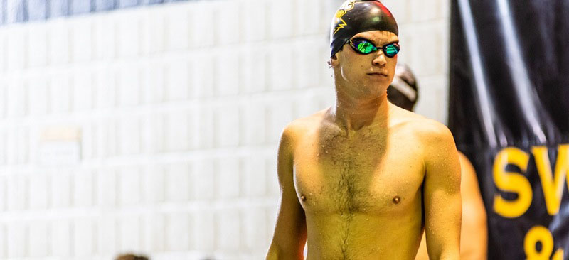Close-up of swimmer standing outside a pool, wearing swim goggles and a swim cap