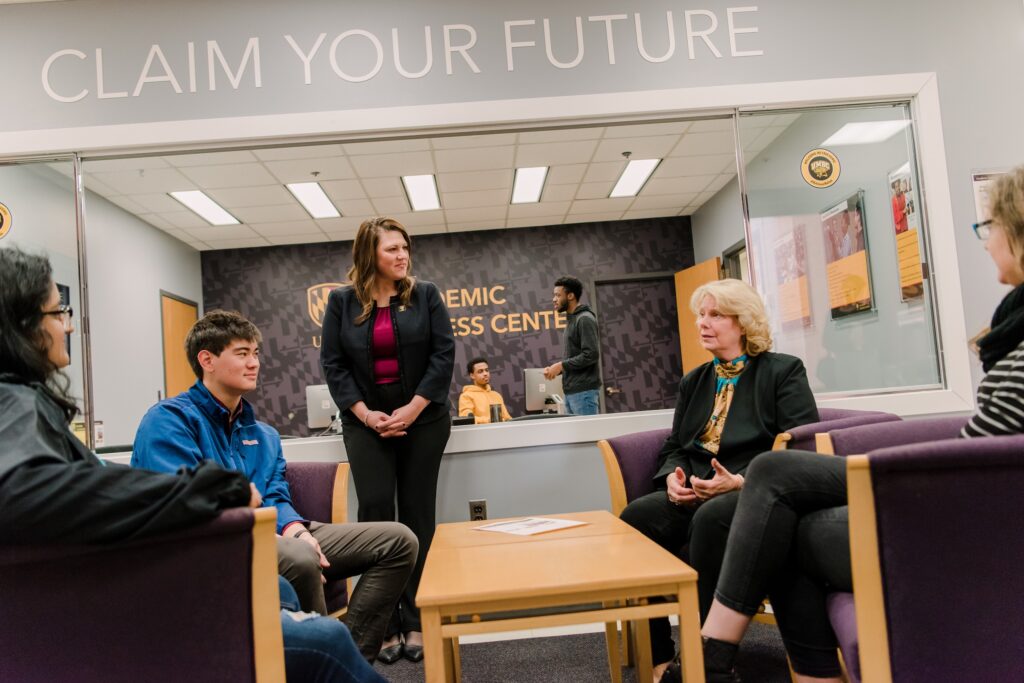 A group of people talks around a table. A sign above them reads "Claim Your Future"
