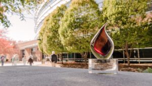 Glass trophy shaped like a flame rests on a concrete surface in front of trees and buildings