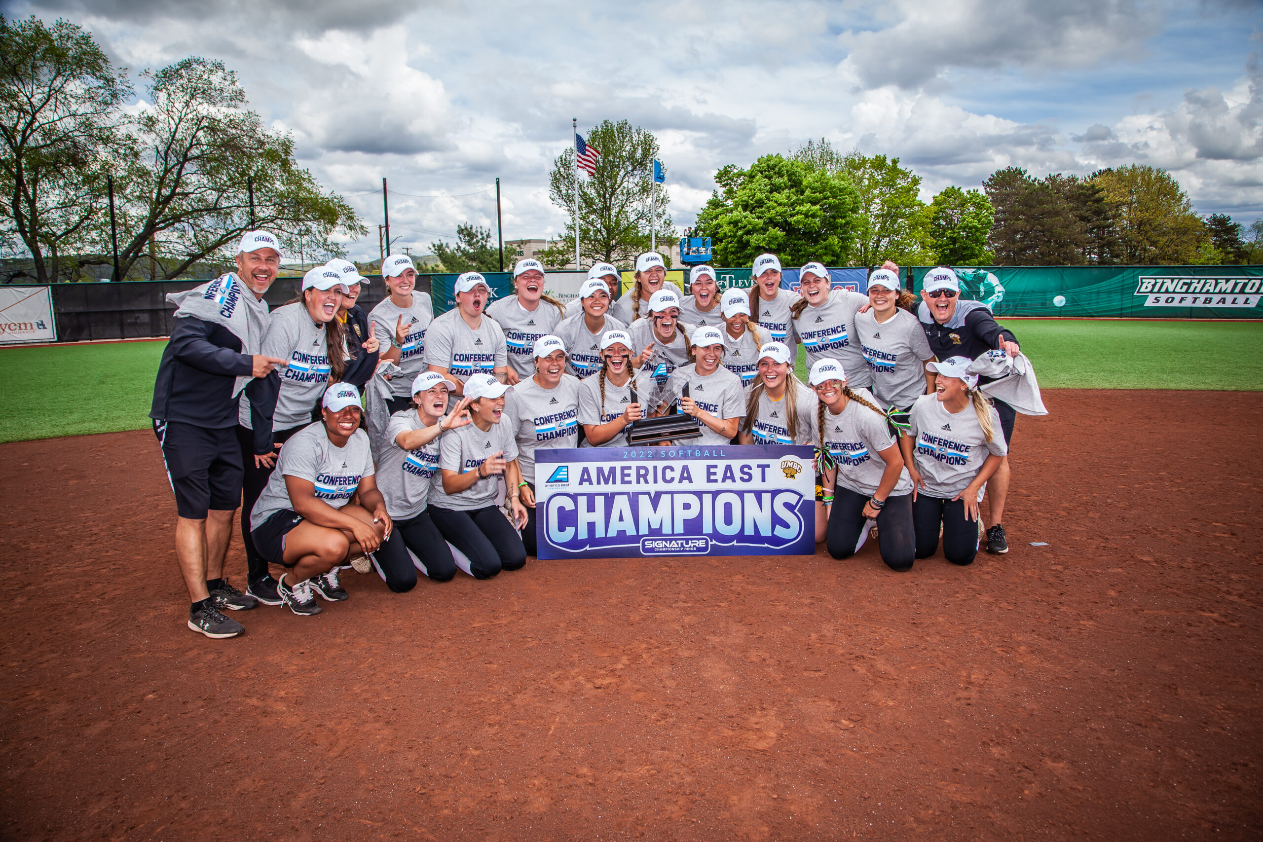 Softball players and coaches huddled around "America East Champions" banner