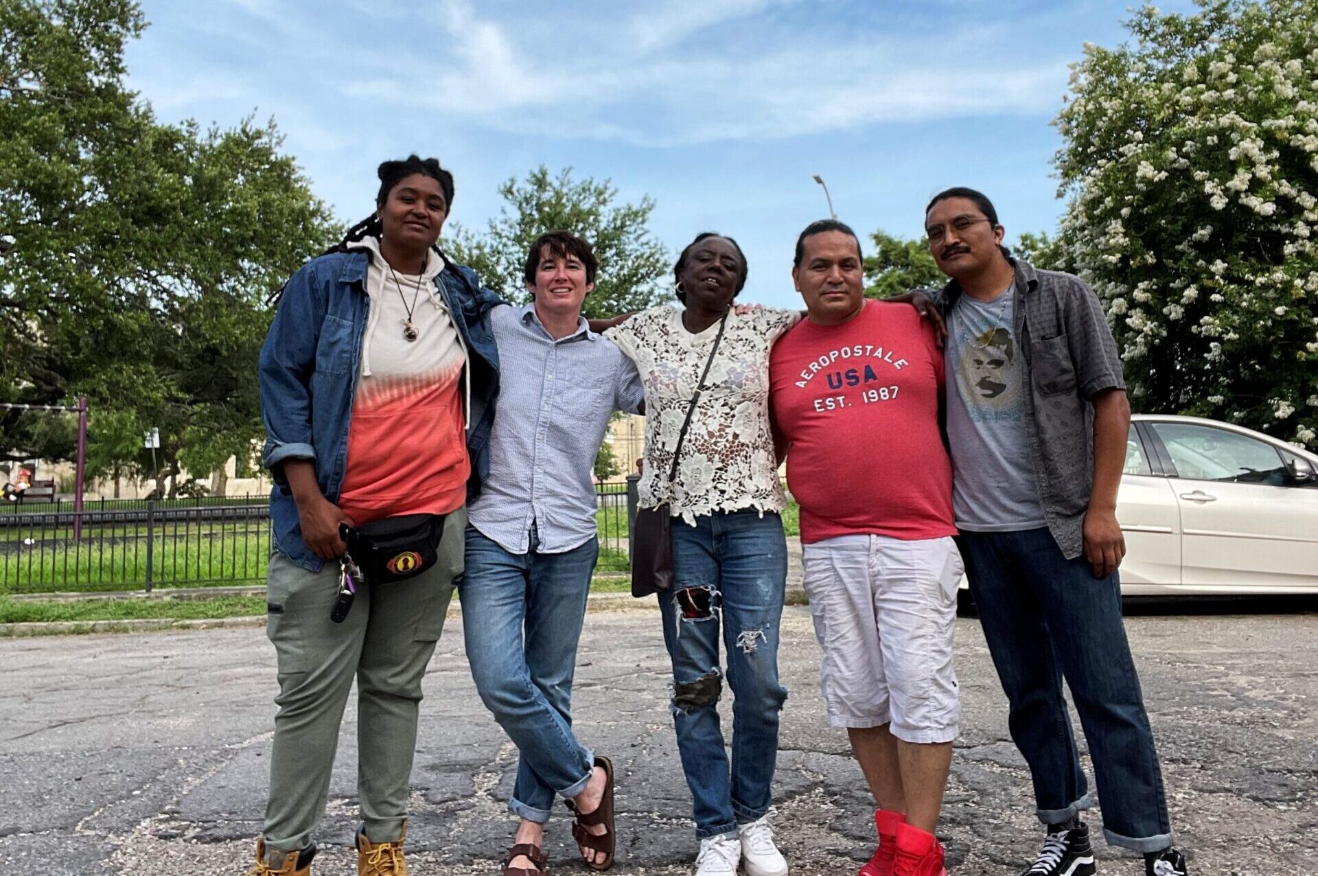 A group of five people standing close together on a street with trees on either side of them.