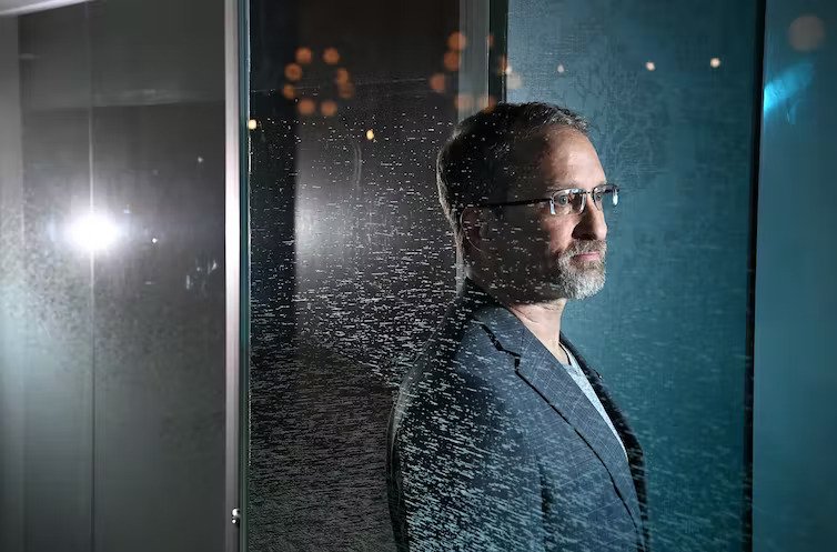 A man with glasses stares through a window pensively