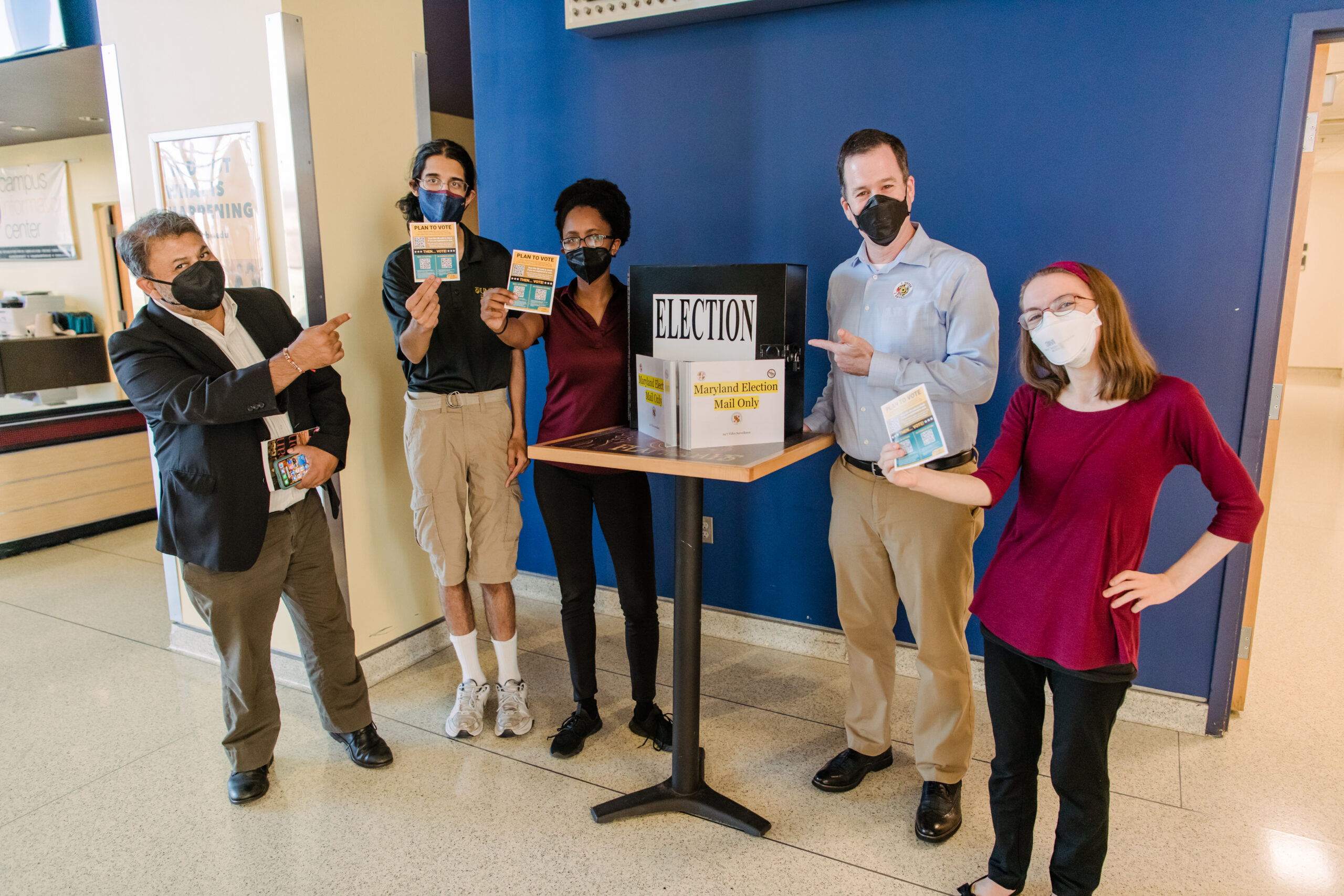 Five people pose next to a mail in ballot drop off box on campus.
