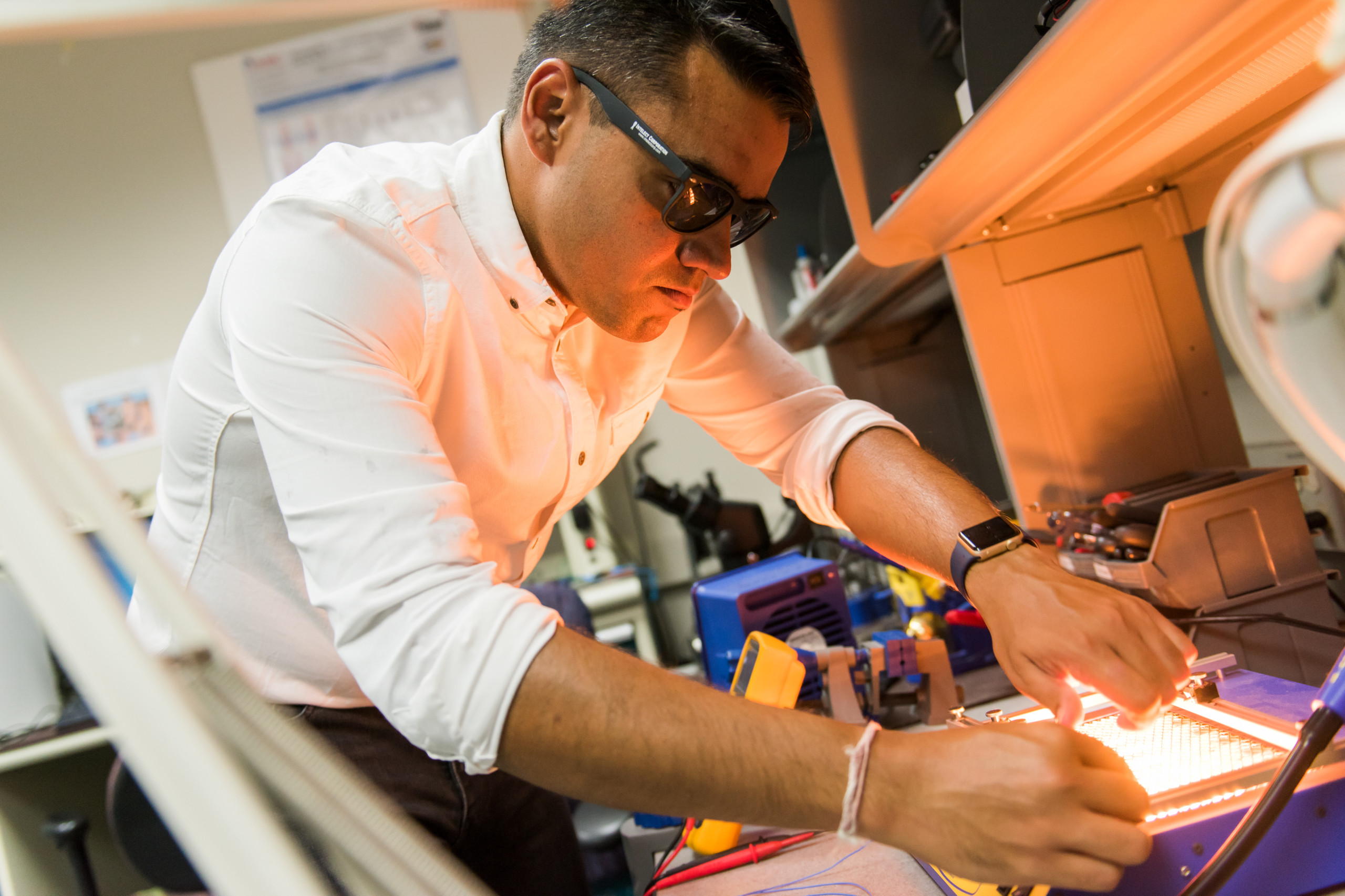 Person working on a machine with a bright light in a lab. They are wearing sunglasses.
