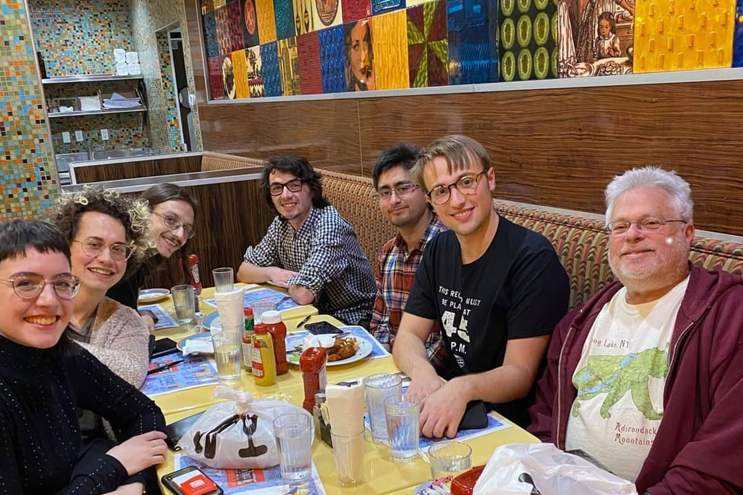 A group of people are seated around a dining table. They smile at the camera.