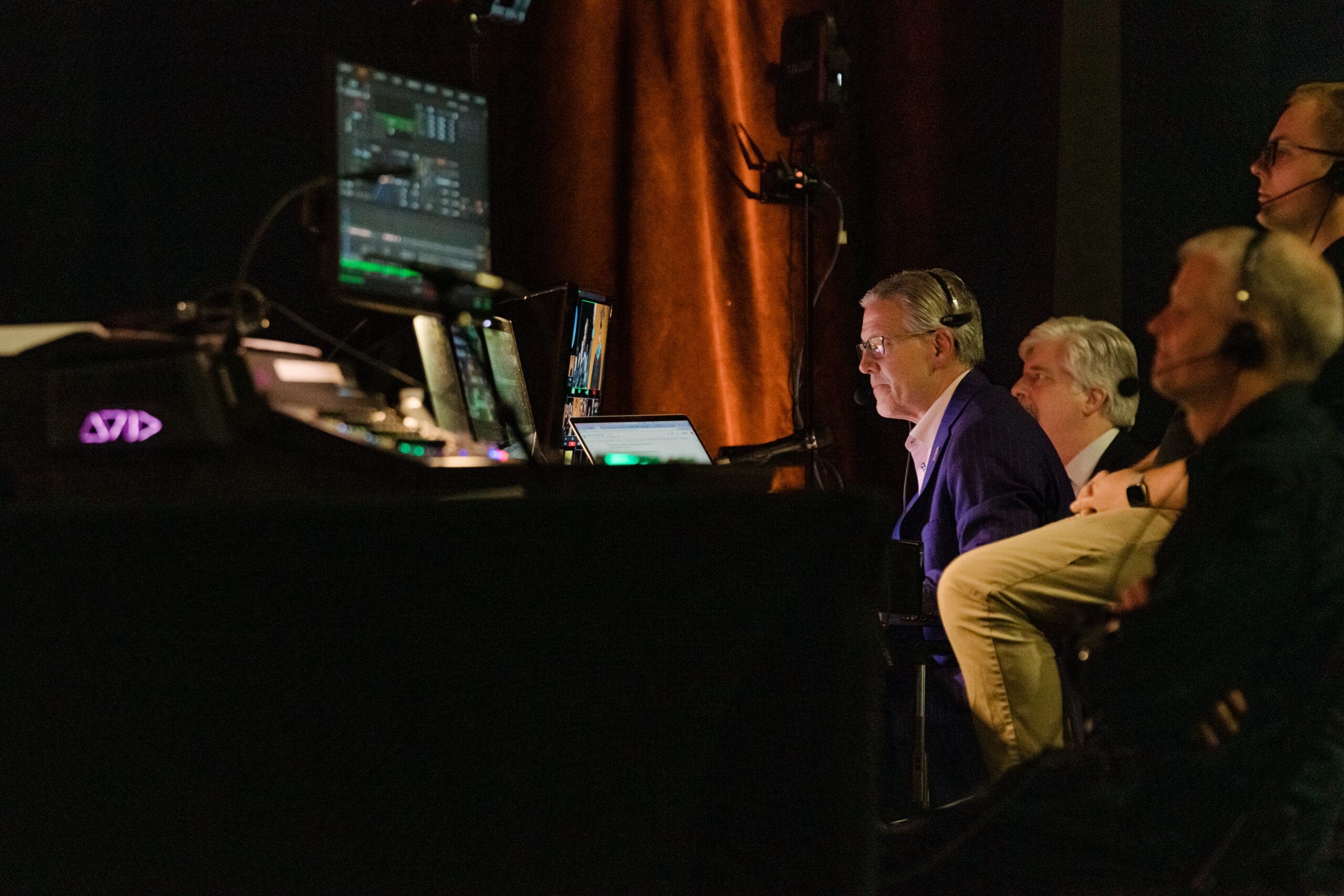 A man sits in a production booth with computer monitors showing him information