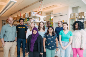 Group photo of nine people in a brightly lit laboratory