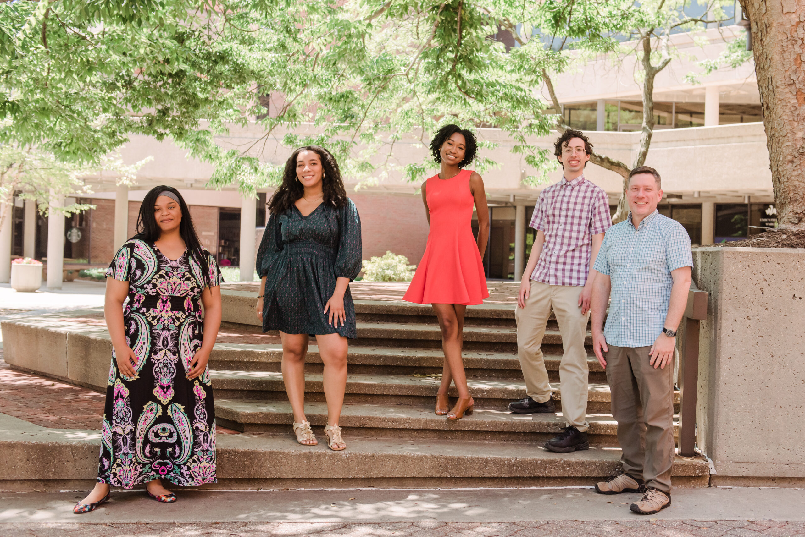 A group of five people stand close to each other on a cement stairwell with trees in the background.
