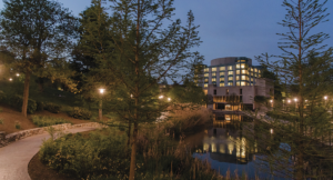UMBC's campus at night, featuring the Albin O. Kuhn library and reflective pond, with street lamps lighting a path.