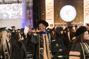 A graduate processes out among other studies smiling