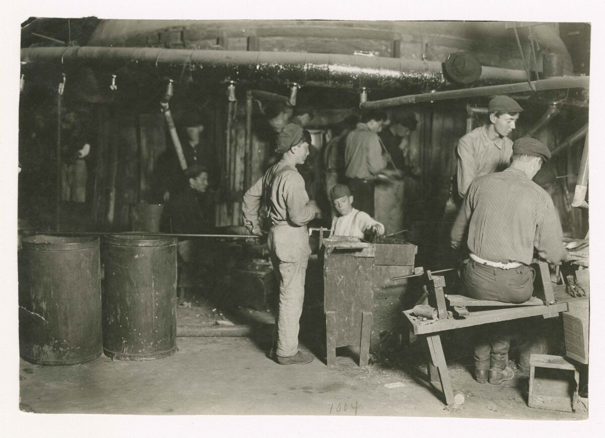 A young child works in a glass factory in a 1909 black and white historical photo by lewis hine