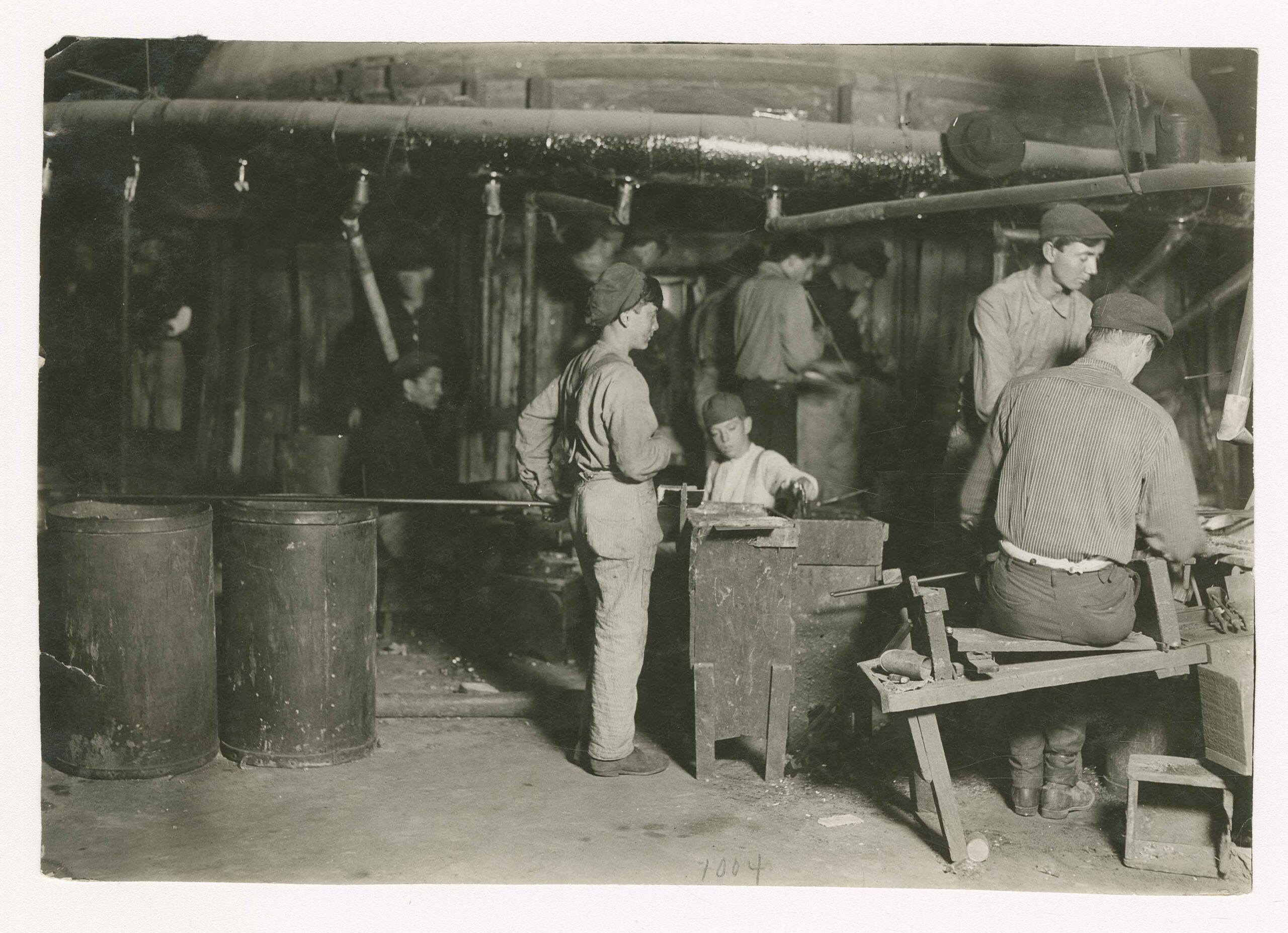 A young child works in a glass factory in a 1909 black and white historical photo by lewis hine
