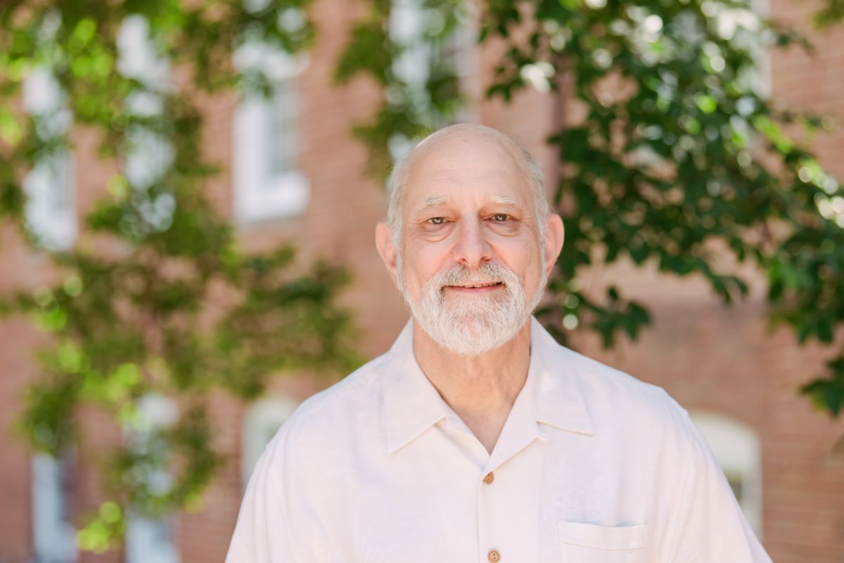 Man stands in front of brick building, smiles at camera