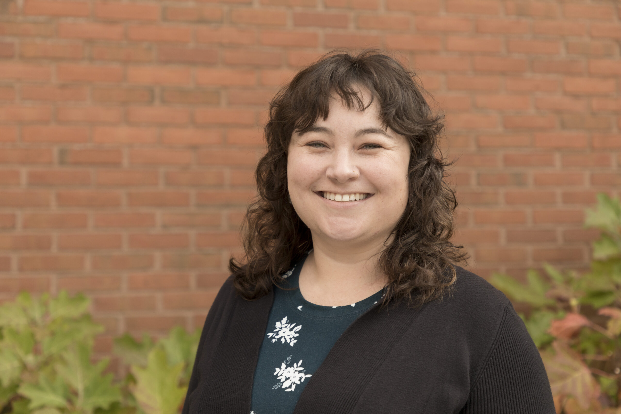 headshot of a woman with curly brown hair in front of a brick wall