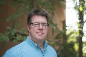 Headshot of man in front of brick building.