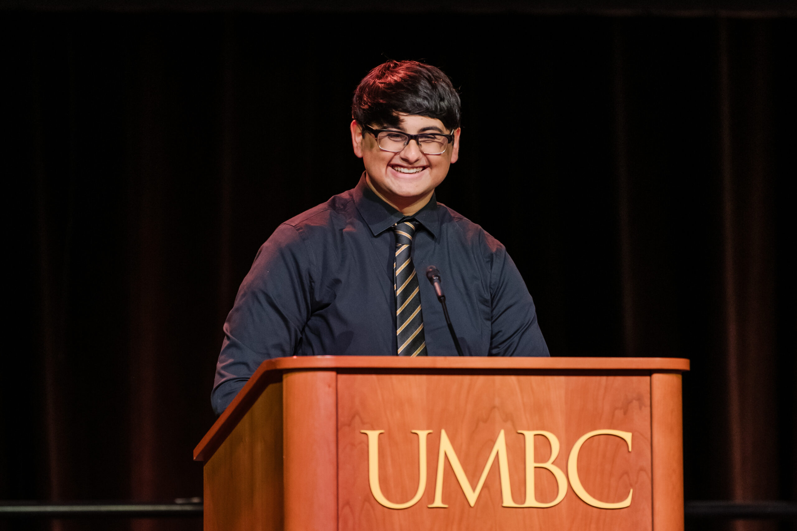 Man standing behind UMBC podium, smiling.