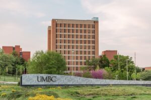 Tall brick building with UMBC sign in foreground. Spring foliage.