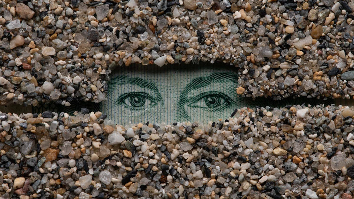 In a work of art, two eyes gaze out from a rectangular enclosure surrounded by small stones.