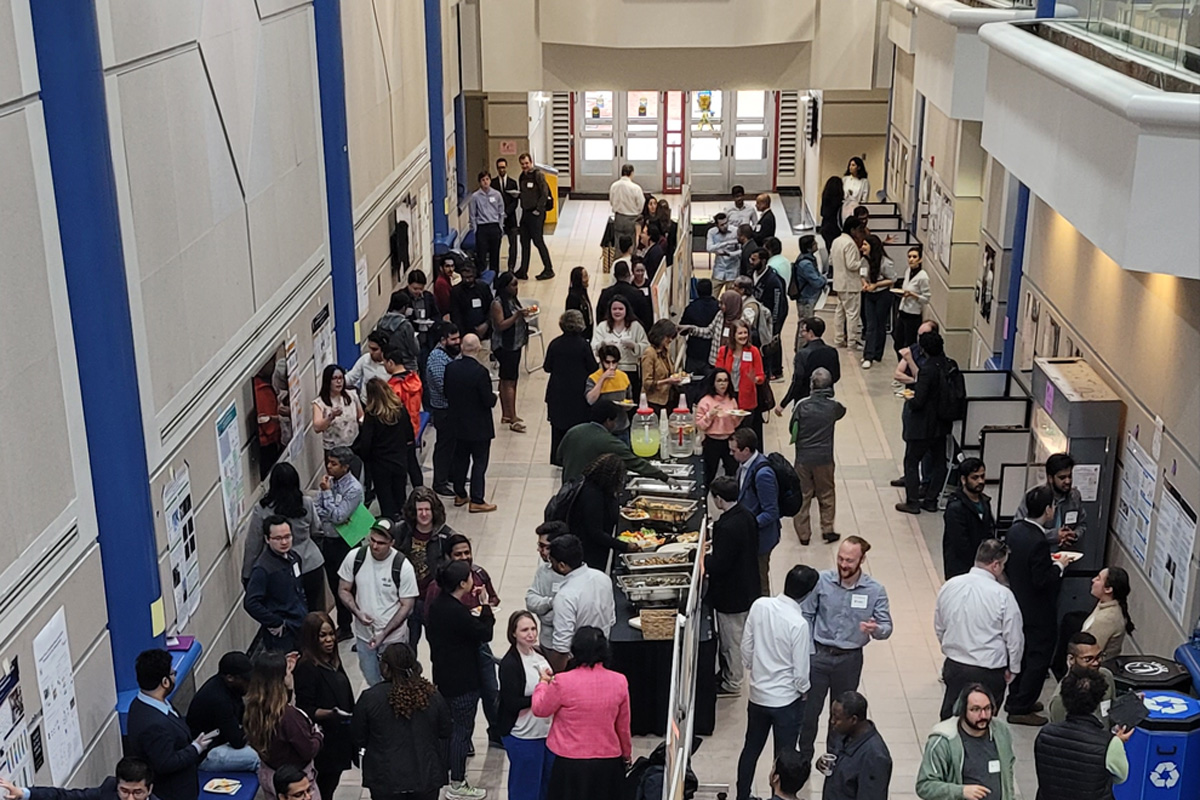 People mingle in large open space. Buffet in center and posters line the wall.