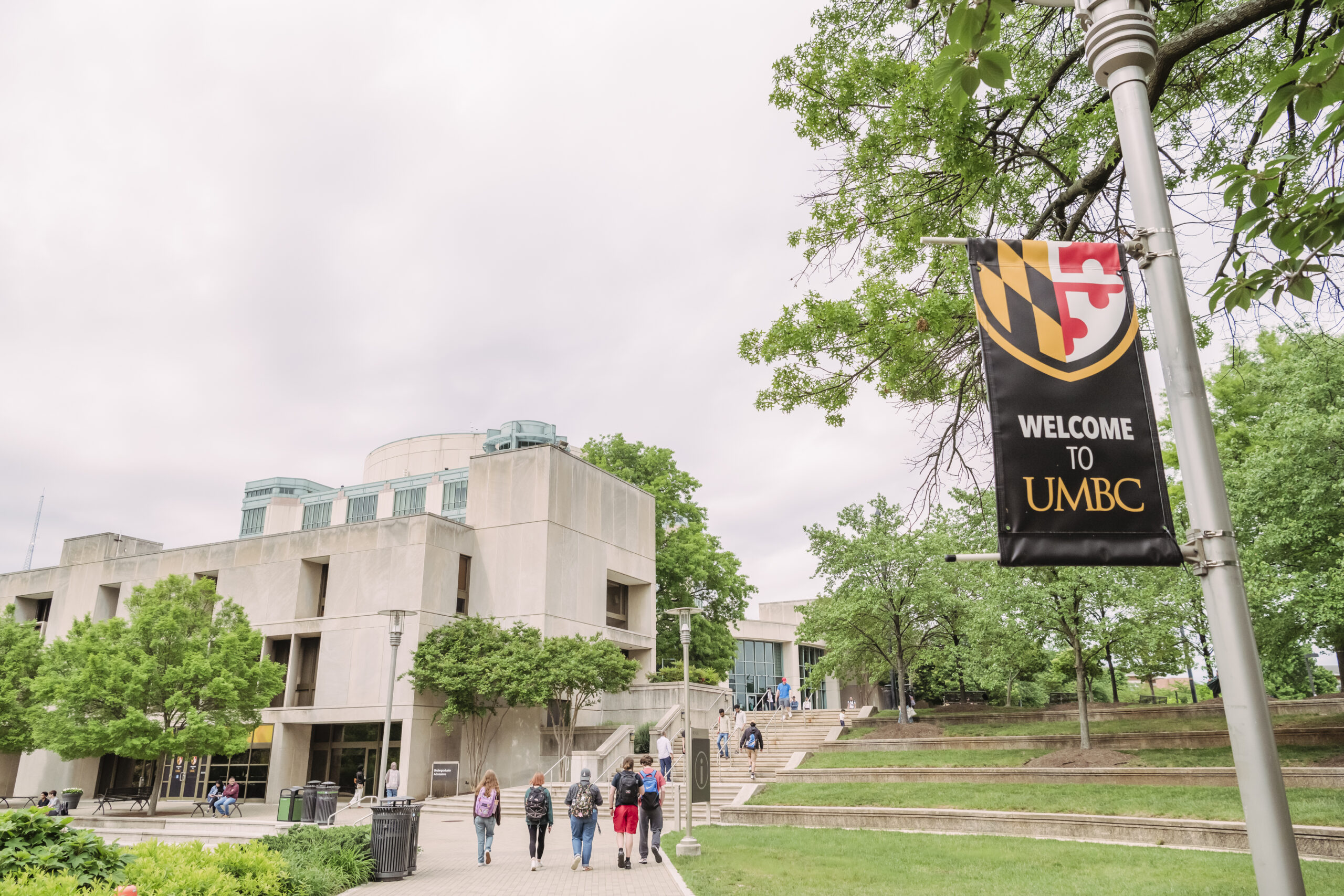 students walk on campus and a sign says Welcome to UMBC