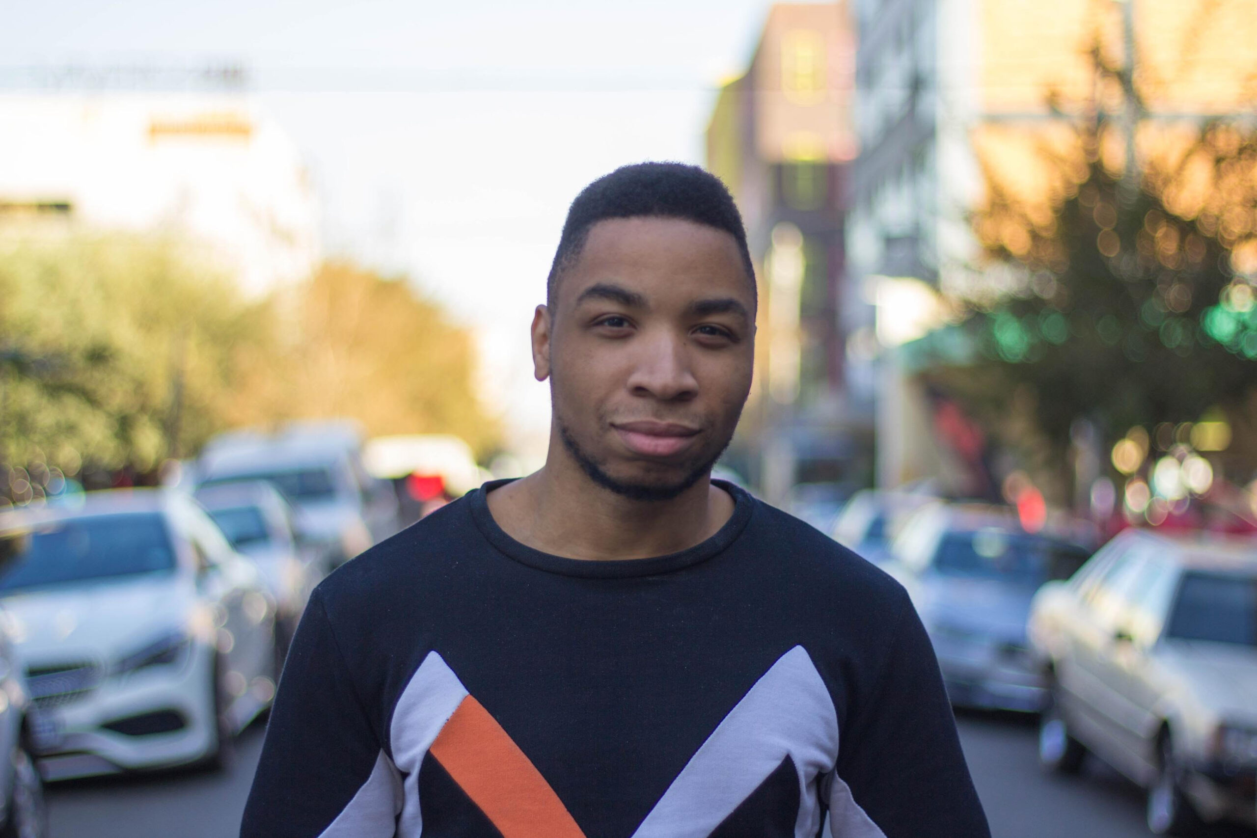 Artist Levester Williams staring into the camera with a blurred image of the street behind him.
