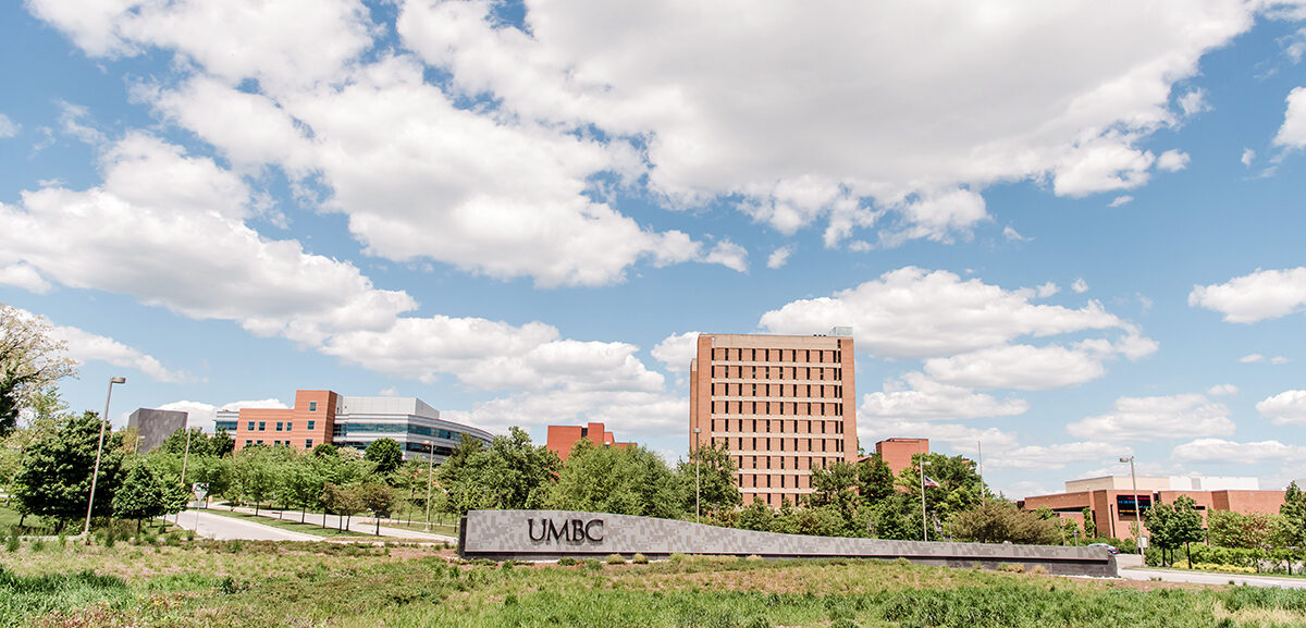 One of the entrances of UMBC's campus. There is a UMBC sign in front of a tall building. The sky is blue and clouds are in the sky. UMBC announces partnership with national nonprofit. incarcerated students program in Maryland