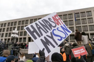 Protestors in front of building. Signs read "Hands off my SSN" and "Hands off workers data"