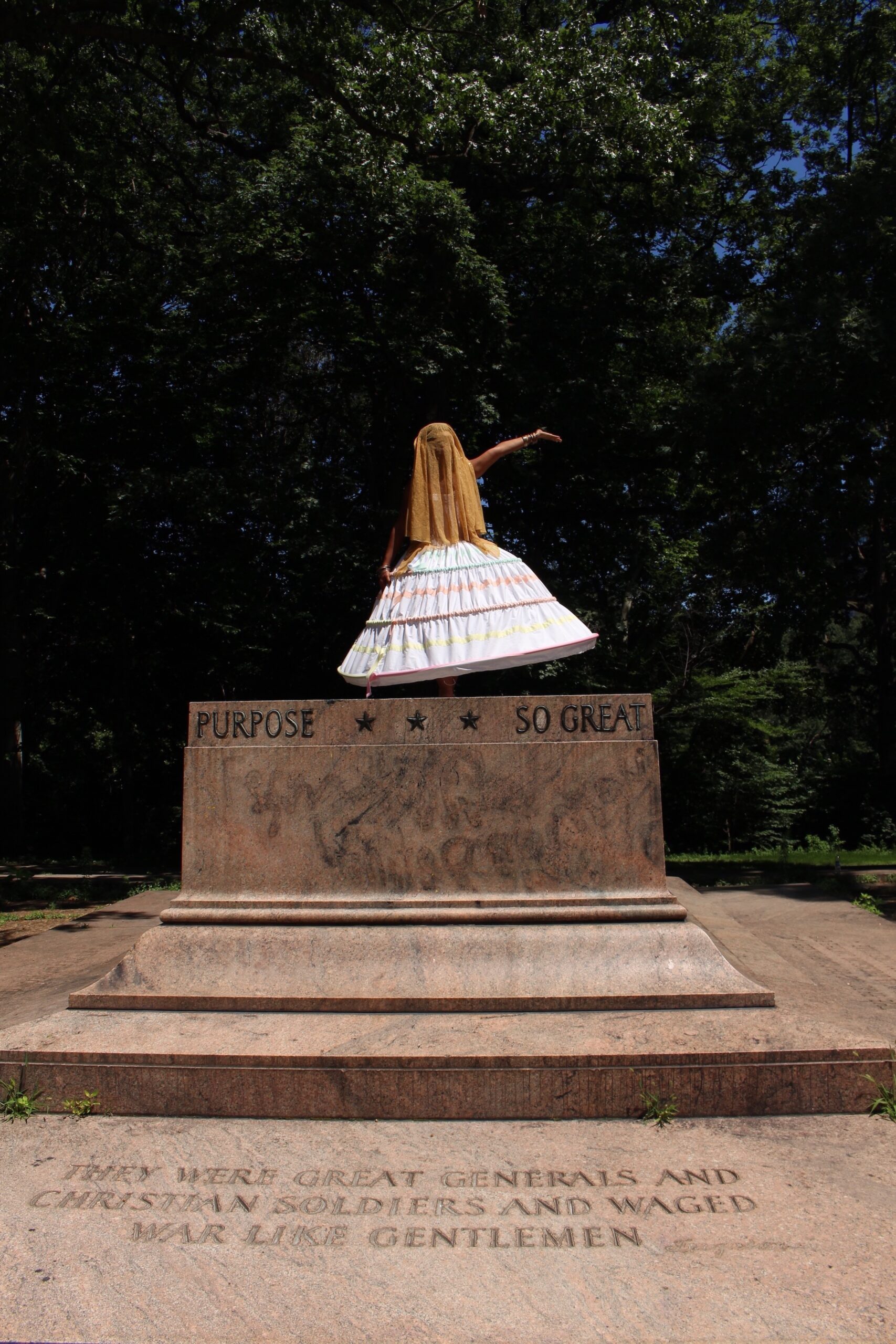 In a costume that obscures her face, Ada Pinkston stands and gestures on the base of a former Confederate memorial.