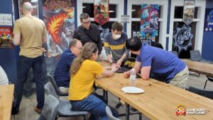 People gather around a table with a laptop in a game store, surrounded by gaming posters.