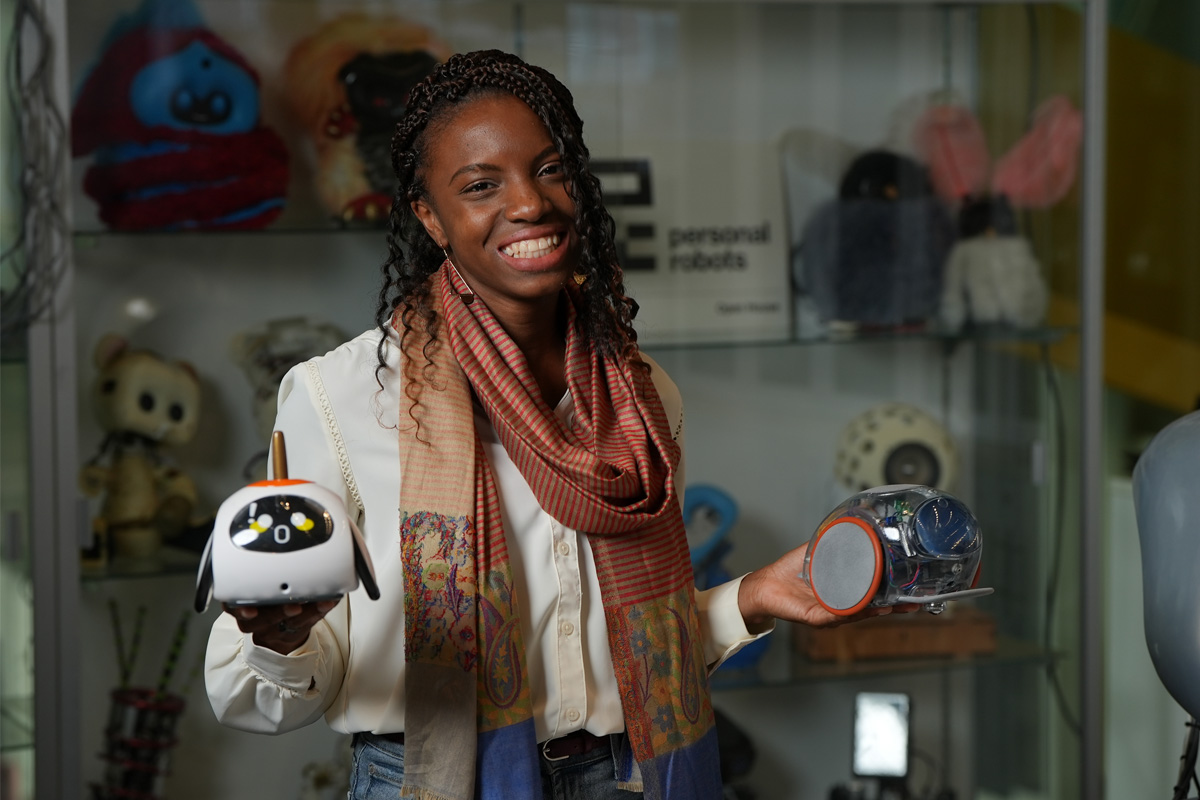 Woman in scarf holds a robot in each hand; smile at camera.