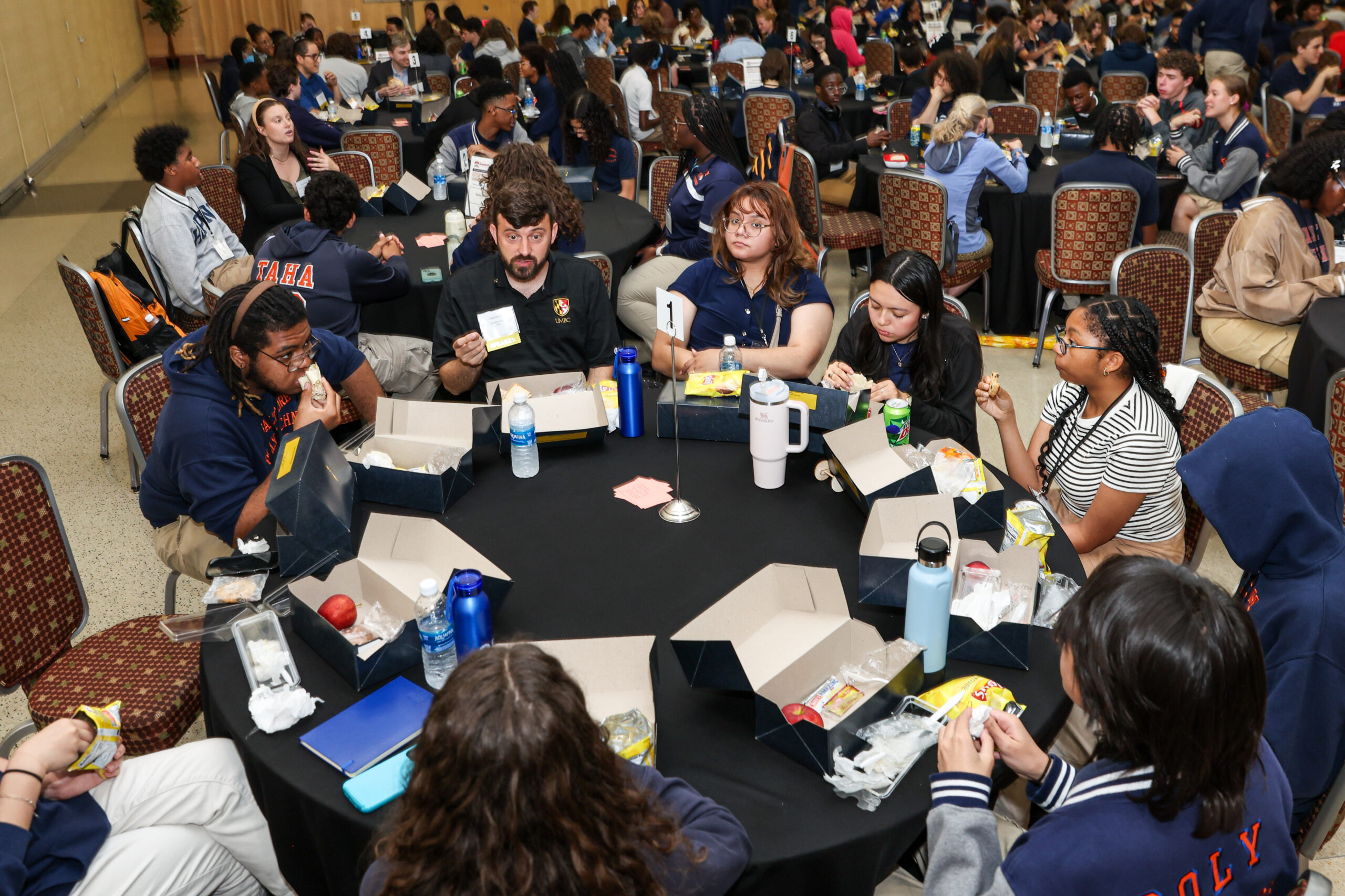 view from above, many students in conversation and eating lunch at many large round tables with black tablecloths
