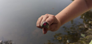 a kid's hand shows a ring with a red gem above a body of water