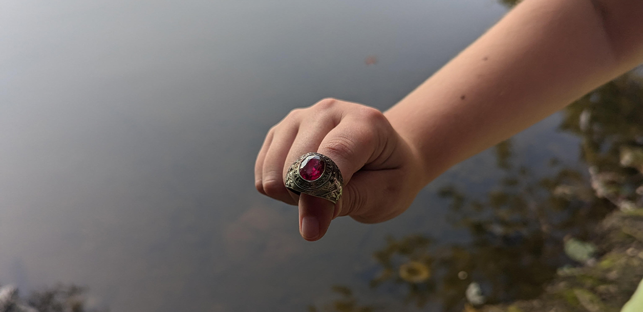 a kid's hand shows a ring with a red gem above a body of water