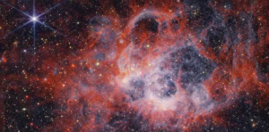 a telescope image of a primarily red, smoky-looking sky region with a bright, six-pointed star in the upper left and many smaller orange and red stars throughout the field of view